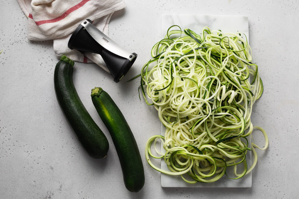 dovlecei intregi si spiralizati in spaghete pe o masa alaturi de un spiralizator