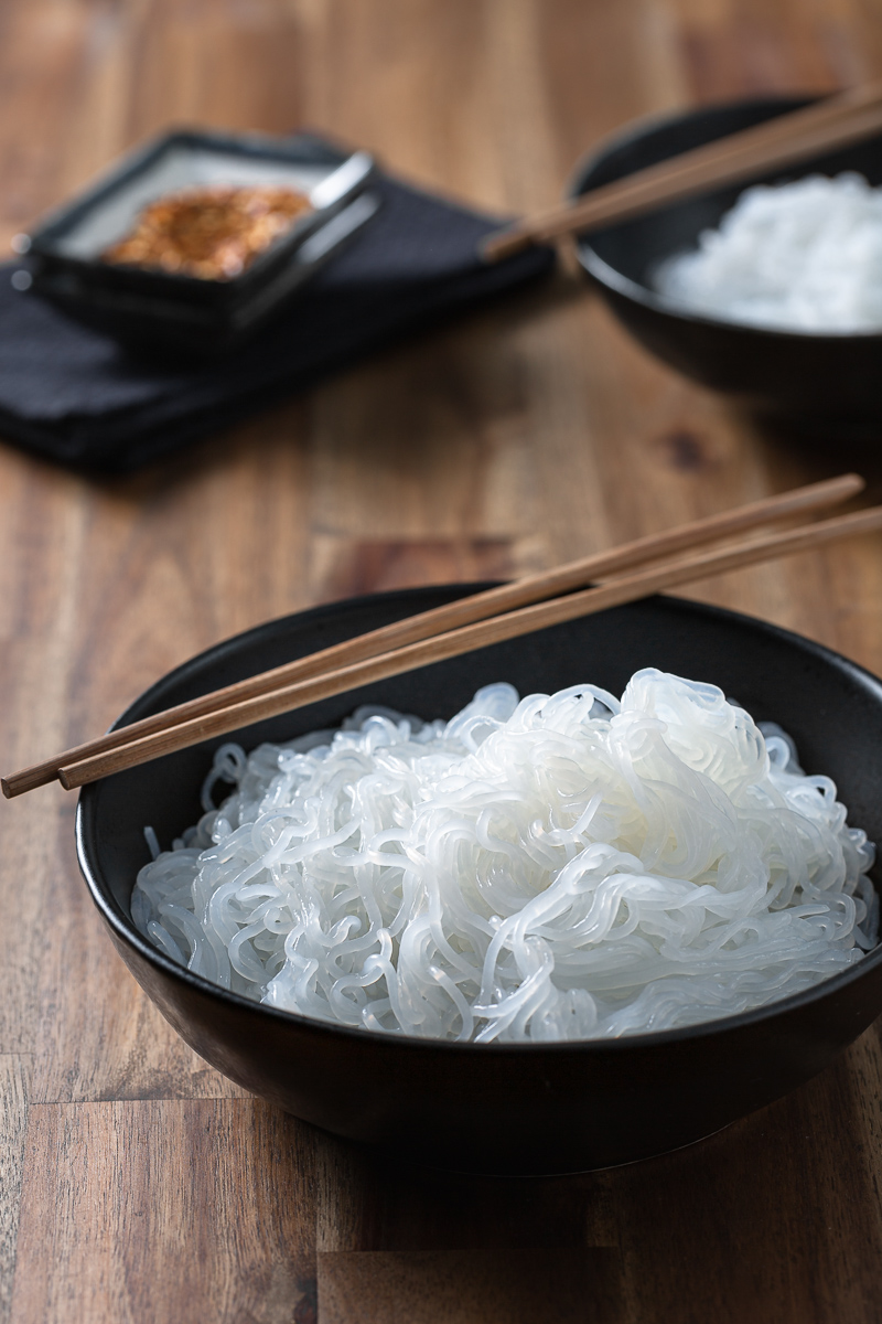 taitei shirataki in castroane negre pe masa cu betisoare chinezesti si fulgi de chili