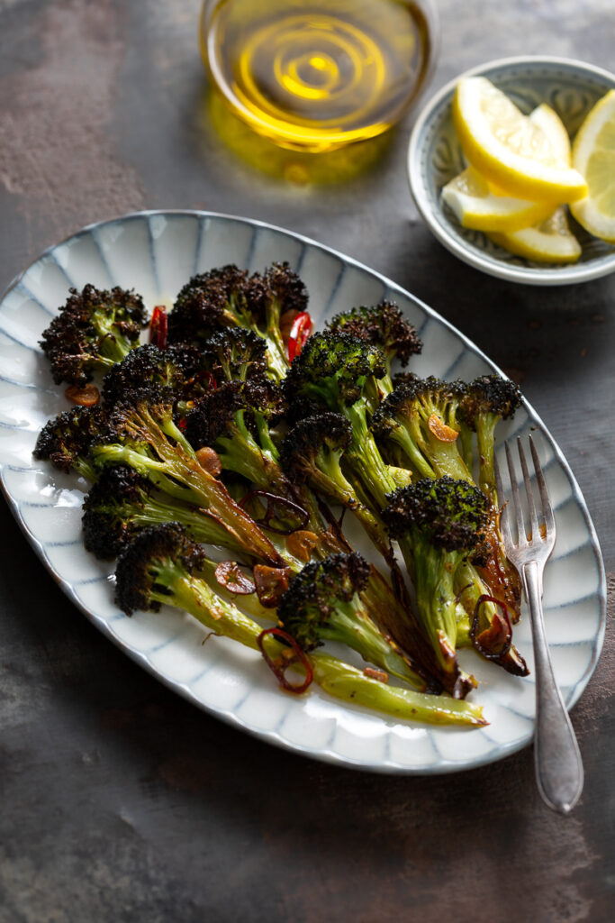 buchetele de broccoli prajit la cuptor cu usturoi si chili pe un platou de servit, cu felii de lamaie si ulei de masline