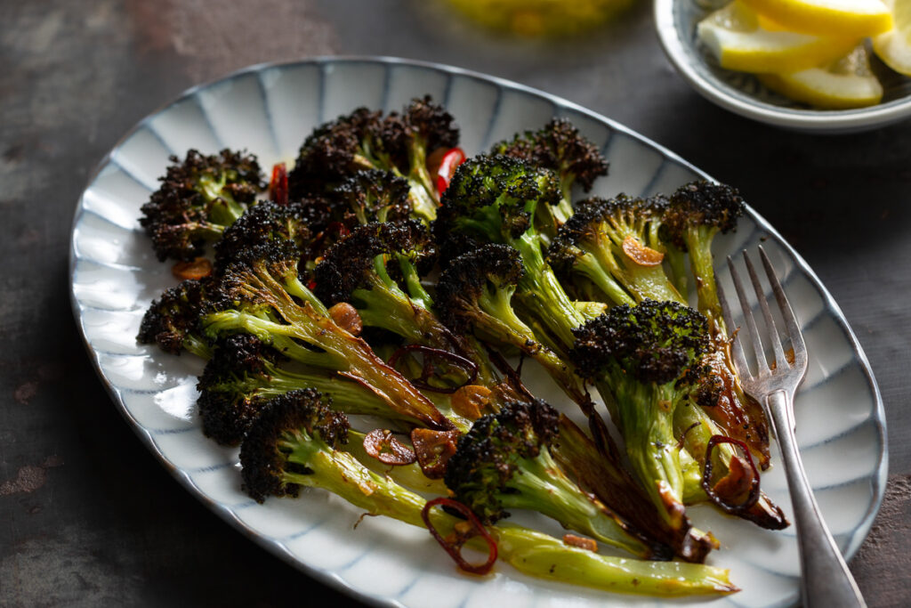 buchetele de broccoli prajit la cuptor cu usturoi si chili pe un platou de servit, cu felii de lamaie si ulei de masline