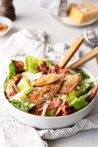 salata Caesar cu dressing home made, piept de pui, bacon si parmezan intr-un bol alb pe masa