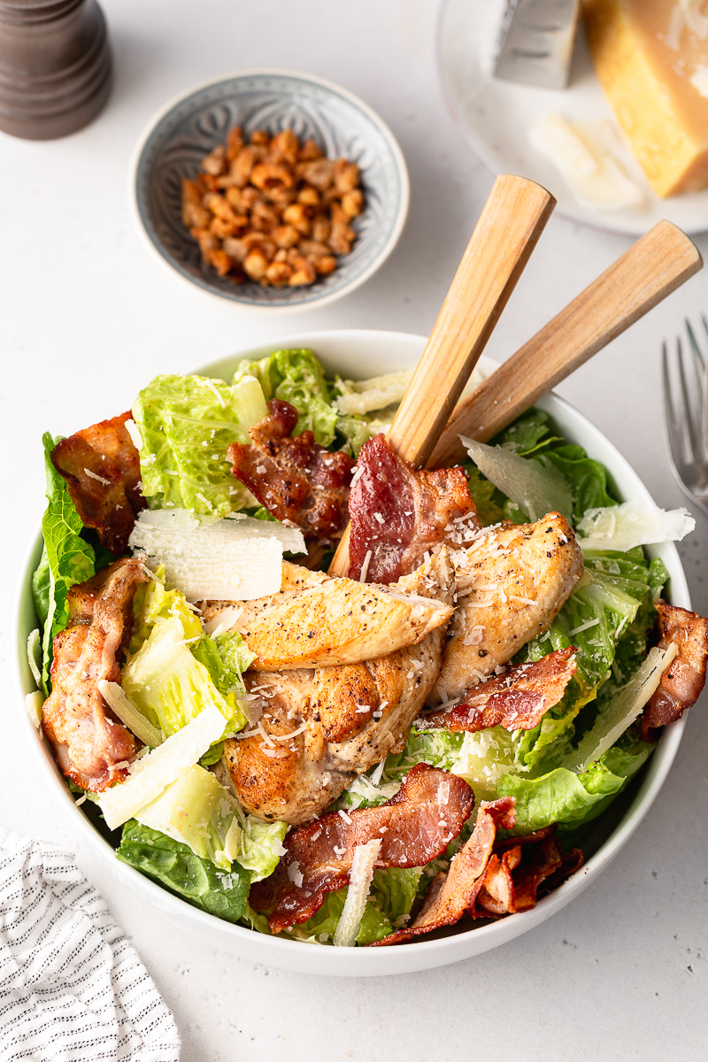 salata Caesar cu dressing home made, piept de pui, bacon si parmezan intr-un bol alb pe masa