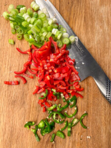 ceapa verde, ardei rosu si jalapeno tocate pe un fund de lemn, alaturi de un cutit