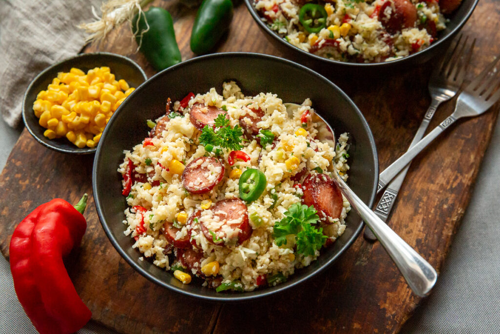 orez mexican din conopida, cu chorizo si legume, jalapeno, porumb, intr-un castron negru