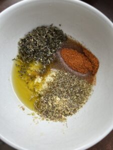 condimente pentru marinada, usturoi, rozmarin, oregano uscat, boia de ardei si ulei de masline intr-un castron