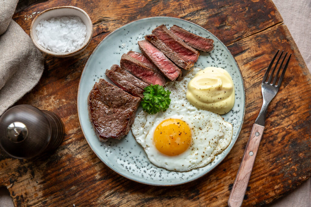 Steak and Eggs keto – friptura felii cu oua si sos olandez pe o farfurie