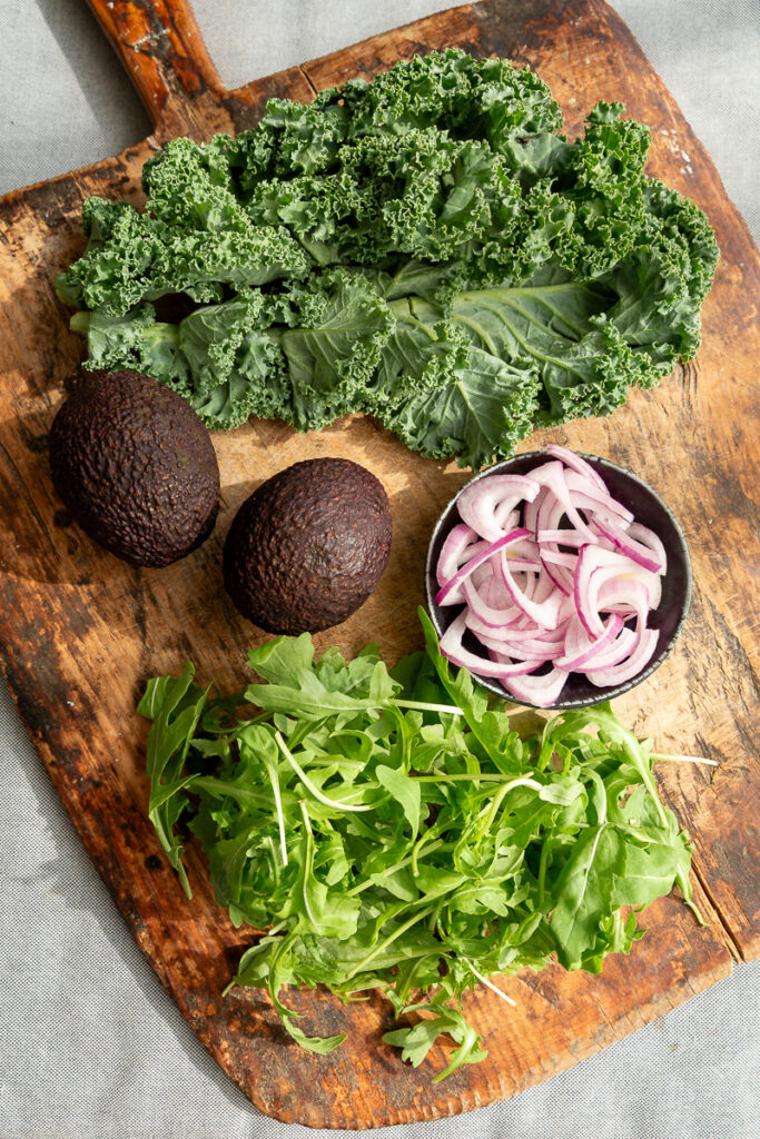 kale, avocado, rucola si ceapa rosie feliata pe un fund de lemn